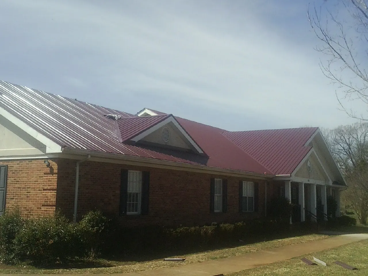 Red metal roof with gabled entries on a long brick building, from a Hail Damage Roof Repair job in Shasta Lake