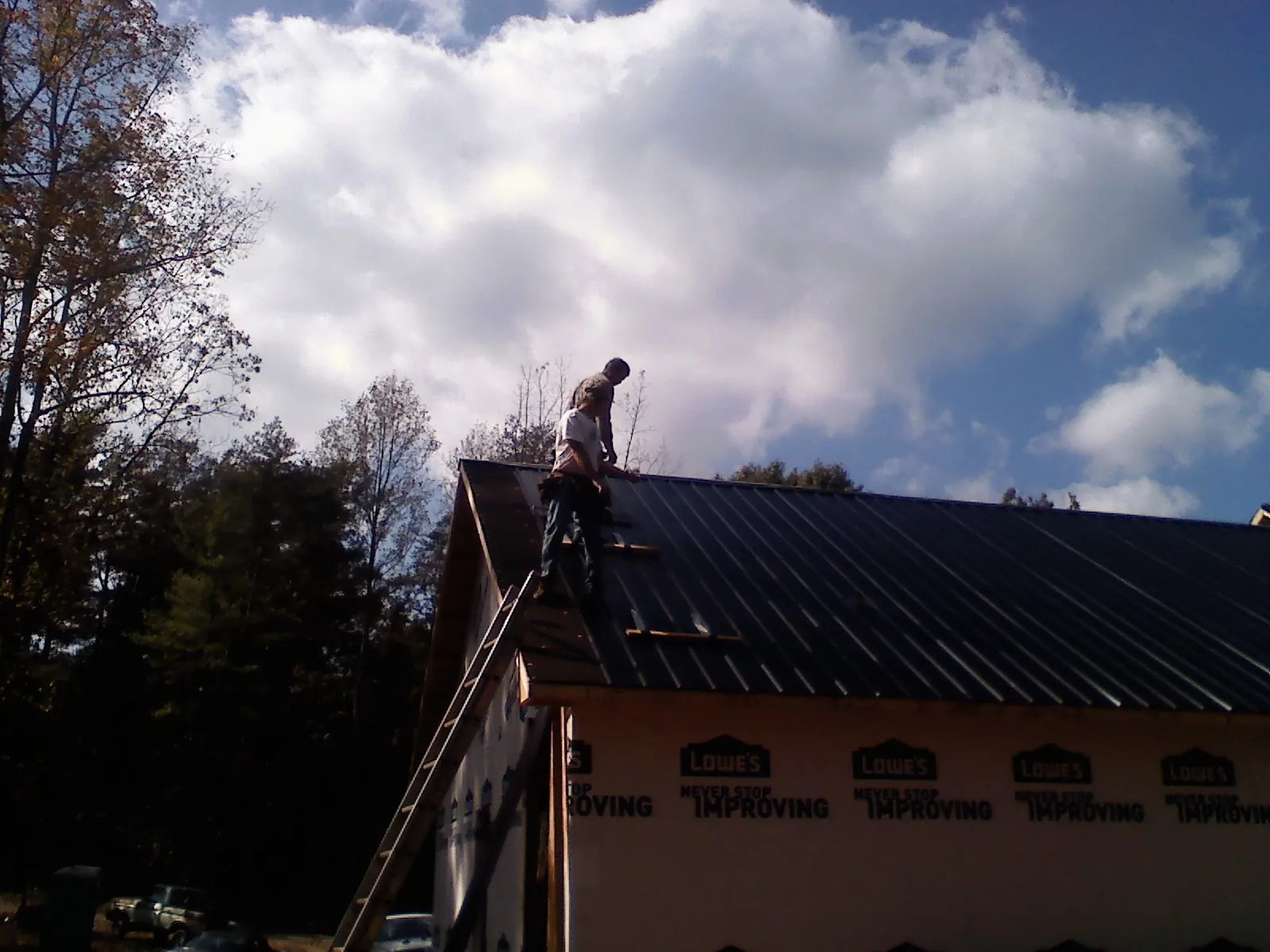 Roofer fastening dark metal panels high against a cloudy sky, from a Roof Inspection job in Shasta Lake