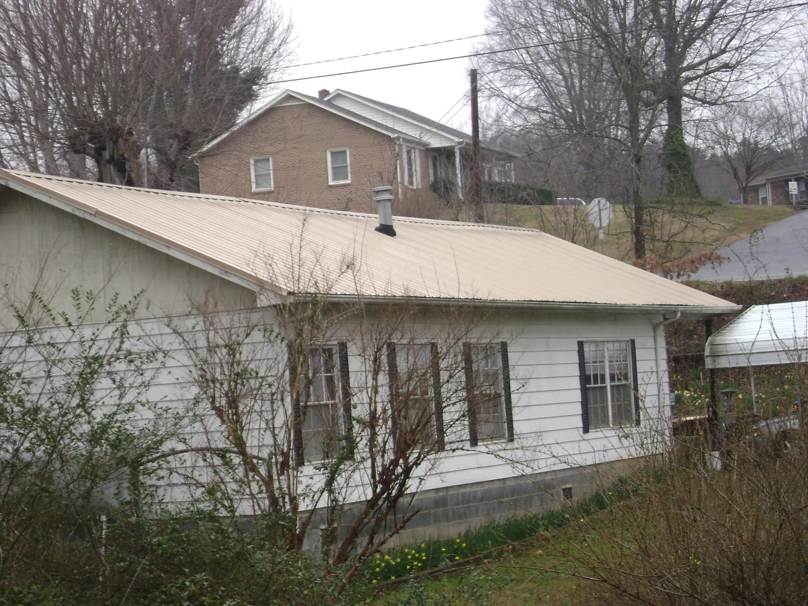 Tan metal roof on a white sided house set into a hillside — Commercial Roofing by Roofing Brothers in Shasta Lake
